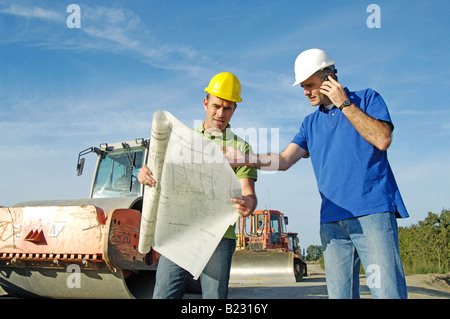 Two male architects discussing blueprints at construction site Stock Photo