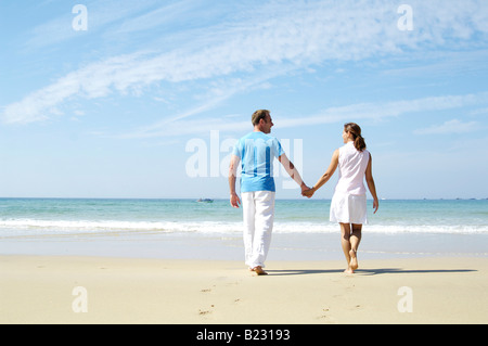 Rear view of couple holding each other's hands and walking on beach Stock Photo