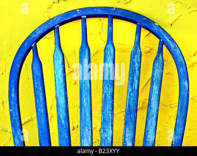 Old blue painted wooden chair leaning against a bright yellow stucco wall Stock Photo
