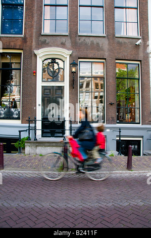 Dutch mother and child riding typical bicycle on canal street in front of Otto Frank historic house where anne frank hid. Stock Photo
