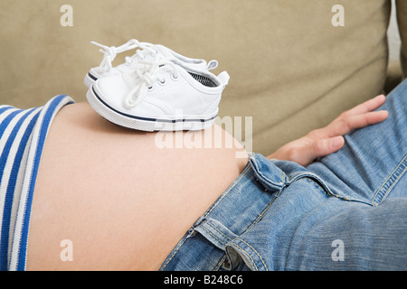 Pregnant woman with baby shoes on stomach Stock Photo