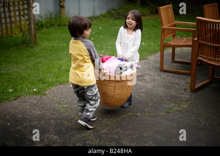 Girl aged five and brother six collect dried washing from line in a basket and bring indoors Stock Photo