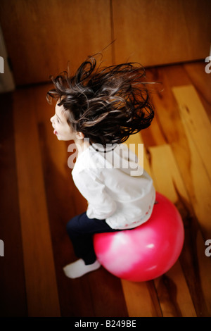 Girl aged five bounces on pink moonhooper indoors Stock Photo