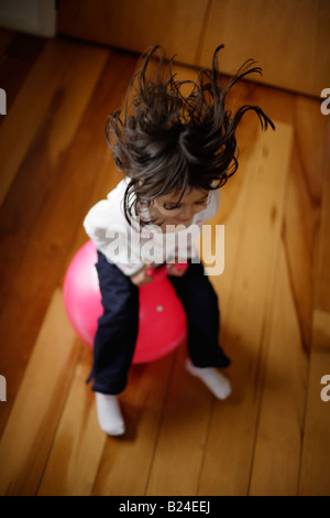 Girl aged five bounces on pink moonhooper indoors Stock Photo