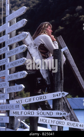 Girl contemplating Signage to various locations around Fiordland, Gun's Camp, Hollyford Valley, New Zealand Stock Photo