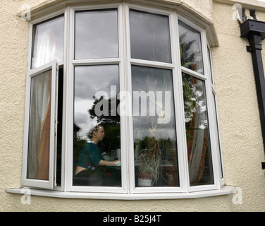 Woman working on a Computer in a surburban House seen through the bay window Stock Photo