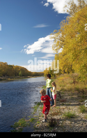 Family Throwing Stones Manuherikia River and Autumn Trees Alexandra Central Otago South Island New Zealand Stock Photo