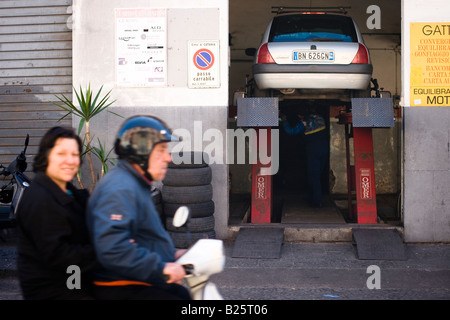 Elderly sicilian couple rides a motorbike past a garage in Catania, Sicily, Italy Stock Photo