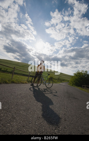 Cyclist standing with bike on road beneath cloudy sky