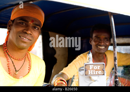 Two men sit in an autorickshaw and smile. They are dressed in yellow due to their participation in a religious festival. Stock Photo