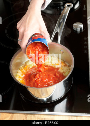 Preparing Delicious Homemade Italian Minced Beef Bolognese Lasagne, Adding A Tin Of Tomatoes To Fried Vegetables On A Hot Kitchen Hob Stock Photo