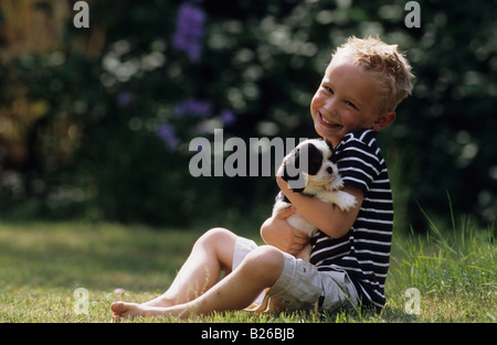 Cavalier King Charles Spaniel (Canis lupus familiaris). puppy in the a arms of a young boy sitting on a lawn Stock Photo