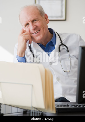 Senior male doctor sitting at desk Stock Photo