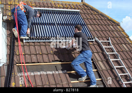 Two solar heating engineers install panels to heat domestic hot water on a roof of a property in Dorset Stock Photo