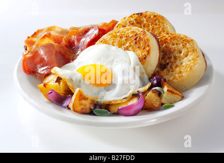 Full English Breakfast with crumpets, served on a white plate in a table setting - Fried egg, bacon, sautéed potatoes and crumpets Stock Photo
