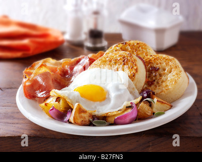 Full English Breakfast with crumpets, served on a white plate in a table setting - Fried egg, bacon, sautéed potatoes and crumpets Stock Photo