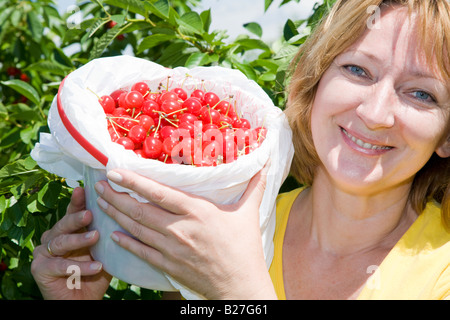 Beautiful smiling woman is holding a bucket full of fresh tart cherries Stock Photo