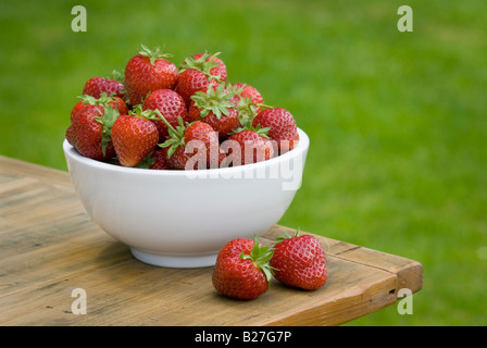 A bowl of freshly picked strawberries on a wooden table outside