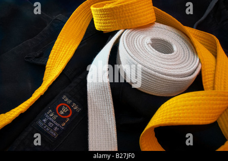 White and yellow karate belts coiled on a folded black gi Stock Photo