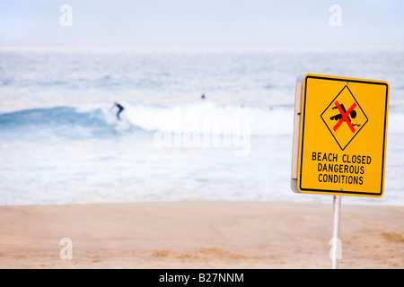 Bronte Beach in winter with few surfers and sign reading: Beach Closed Dangerous Conditions. Stock Photo