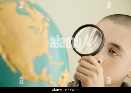 Boy examining globe with magnifying glass Stock Photo