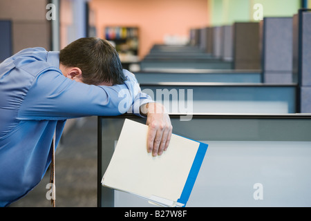 Businessman leaning head on cubicle wall Stock Photo