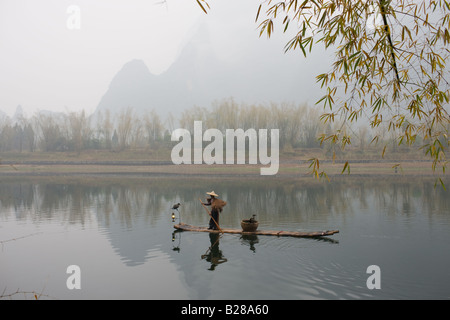 Fisherman in Suoyi coat and coolie hat fishes with cormorants on Li River near Guilin China Stock Photo