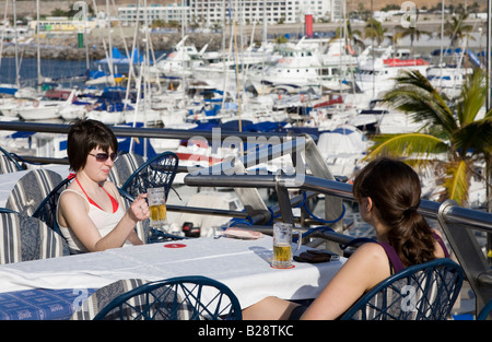 Two girls drinking beer outdoors at marina bar Puerto Rico Gran Canaria Spain Stock Photo