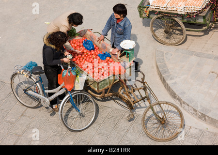 Women buying tomatoes from cart in street market viewed from the City Wall Xian China Stock Photo