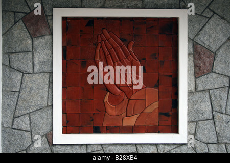 Sculpture of palms joined in prayer as in a photo frame to depict a wall painting on a stone wall of a Church Stock Photo