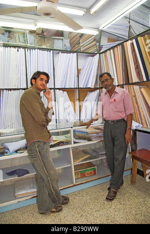 Two Indian tailors in shop with fabric for making traditional Omani robes or dishdashas Barka Oman Stock Photo