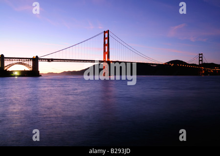 South tower of Golden Gate Bridge glows against beautiful sunset sky with Fort Point lit by fluorescent floodlight Stock Photo