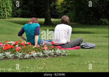 People In The Park: Two young women sit on the grass in Sheffield's Botanical Garden chatting and relaxing over lunch period. Stock Photo