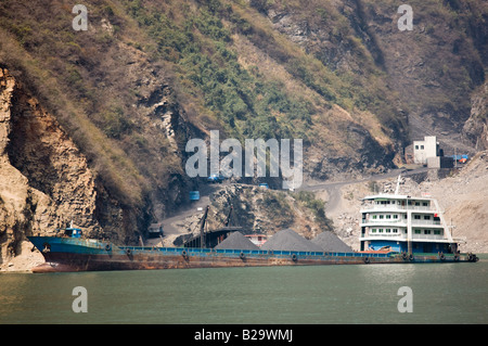 Freight ship being loaded with coal from delivery trucks on the shore in Three Gorges area Yangtze River China Stock Photo