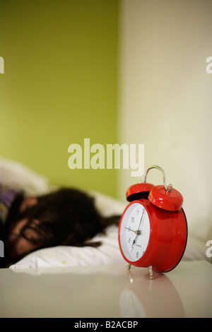 Girl aged five sleeps in her bed beside bright red alarm clock Mixed race indian english