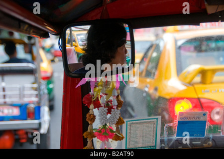 A driver is reflected in the rearview mirror of an Auto rickshaw taxi, commonly known as Tuk Tuk in Bangkok Thailand Stock Photo