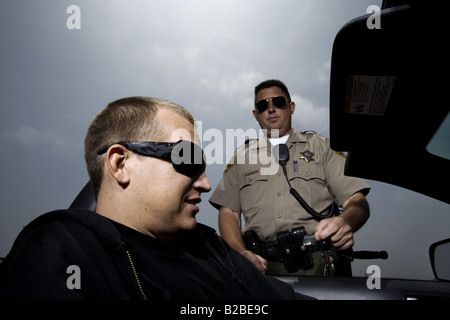 Police officer holding pack of drugs  by man seated in car Stock Photo