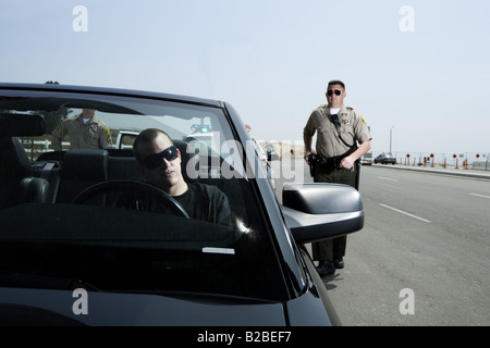 Two police officers approaching man in black Mustang Stock Photo