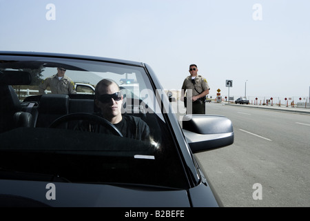 Two police officers approaching man in black Mustang Stock Photo