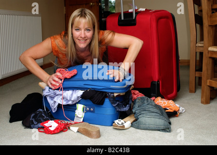 Woman packing and try to close a full holiday suitcase