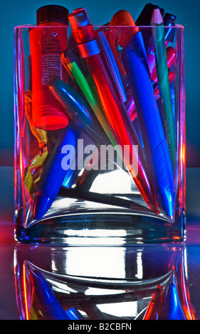 on my desk very colored pens pencils in a glass accumulation bin collecting tank sump Stock Photo