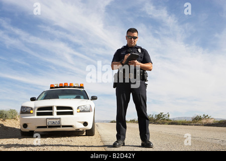 Police officer taking notes in front of police car Stock Photo