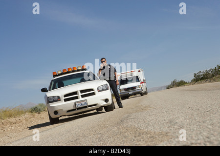 Police officer standing by police car with ambulance in background Stock Photo