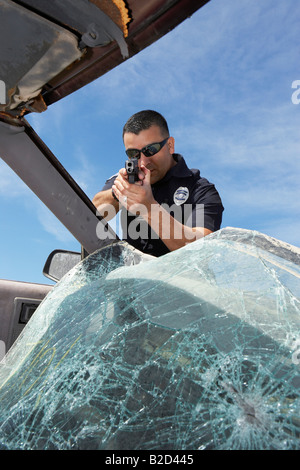 Police officer aiming gun through broken car windshield Stock Photo