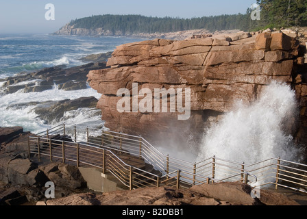 Wave crashing at Thunder Hole, in Acadia National Park.  Red granite in foreground and Otter Cliffs in the background. Stock Photo