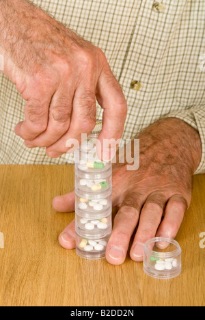 Vertical close up of an elderly gentleman organising his weekly medication into a stacking tower of containers. Stock Photo