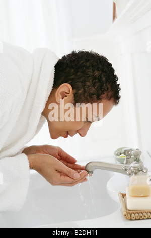 African American woman washing face in sink. Stock Photo