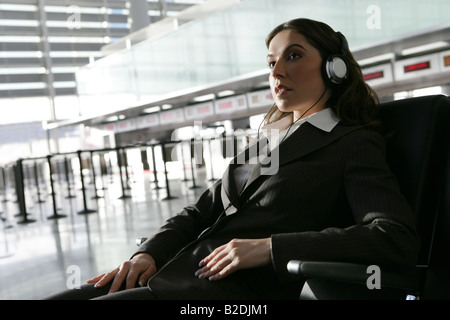 Young businesswoman listening to headphones in airport. Stock Photo