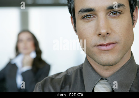Portrait of businessman in airport with businesswoman behind. Stock Photo
