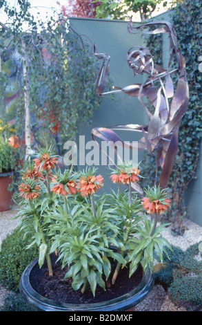 Orange crown imperials in pot in front of modern metal statue Stock Photo